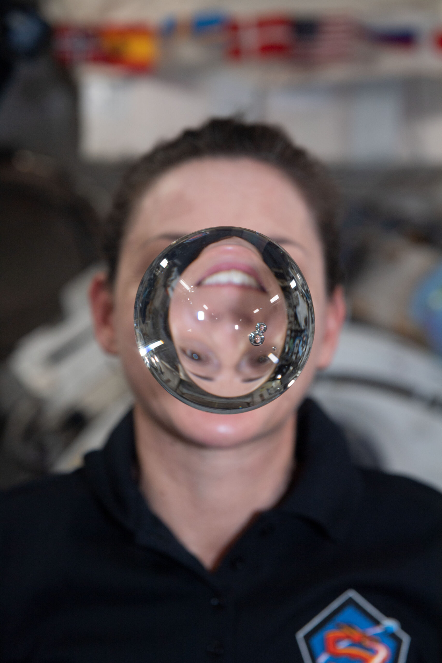 Селфи астронавтки Николь Манн преломляется сквозь плавающий водяной пузырь, летящий в условиях микрогравитации на борту МКС