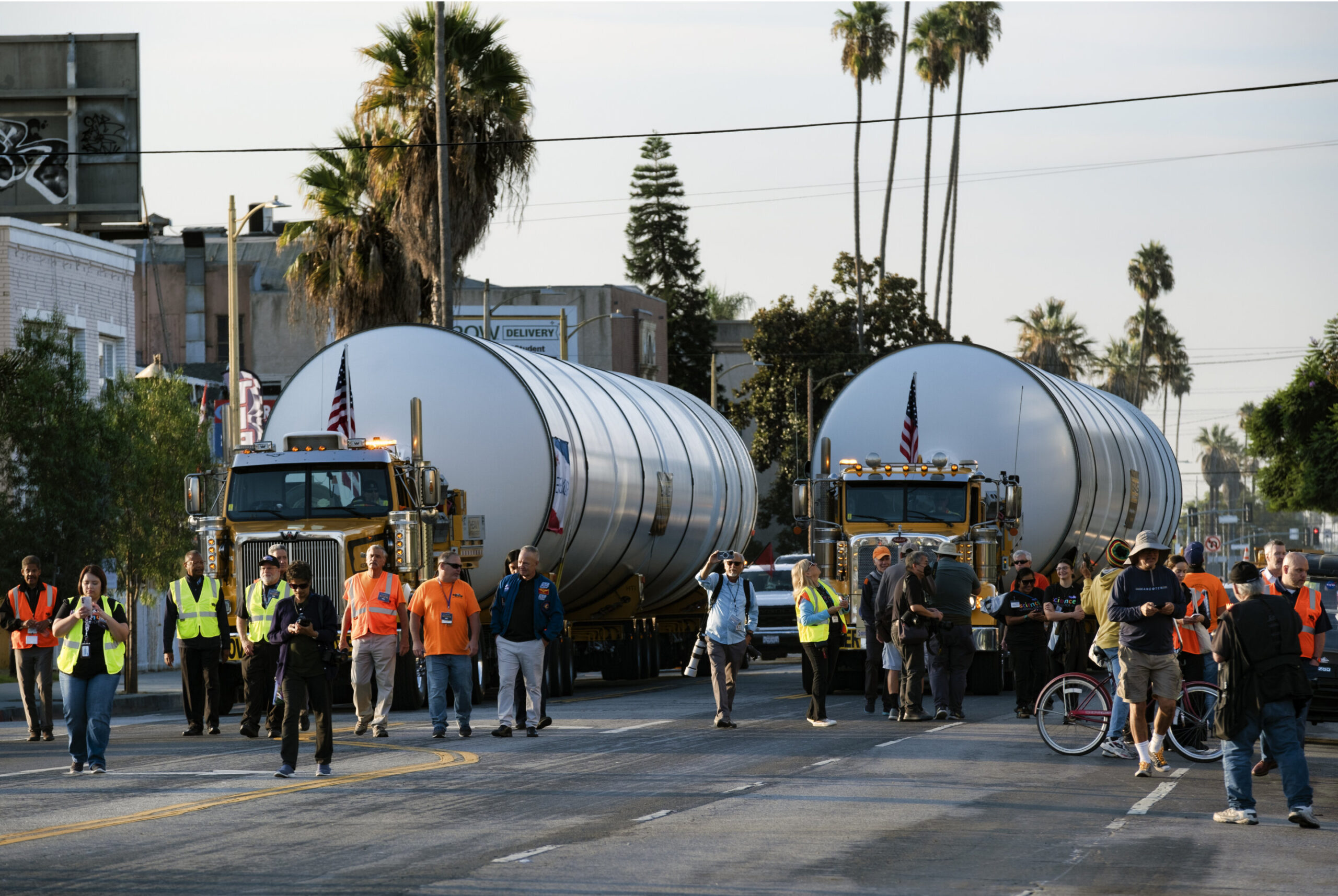 Сотрудники дорожного движения освобождают путь, когда грузовики медленно везут два ракетных двигателя по улице в Лос-Анджелесе