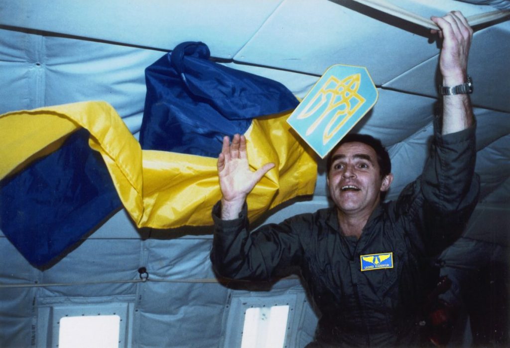 Леонід Каденюк у невагомості тримає герб України поряд з розгорнутим державним прапором на борту шатла Columbia