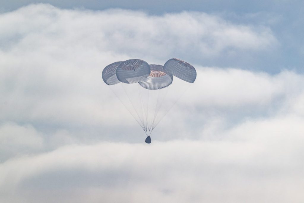 Капсула SpaceX Crew Dragon Freedom під розкритими парашутами опускається до поверхні Тихого океану.